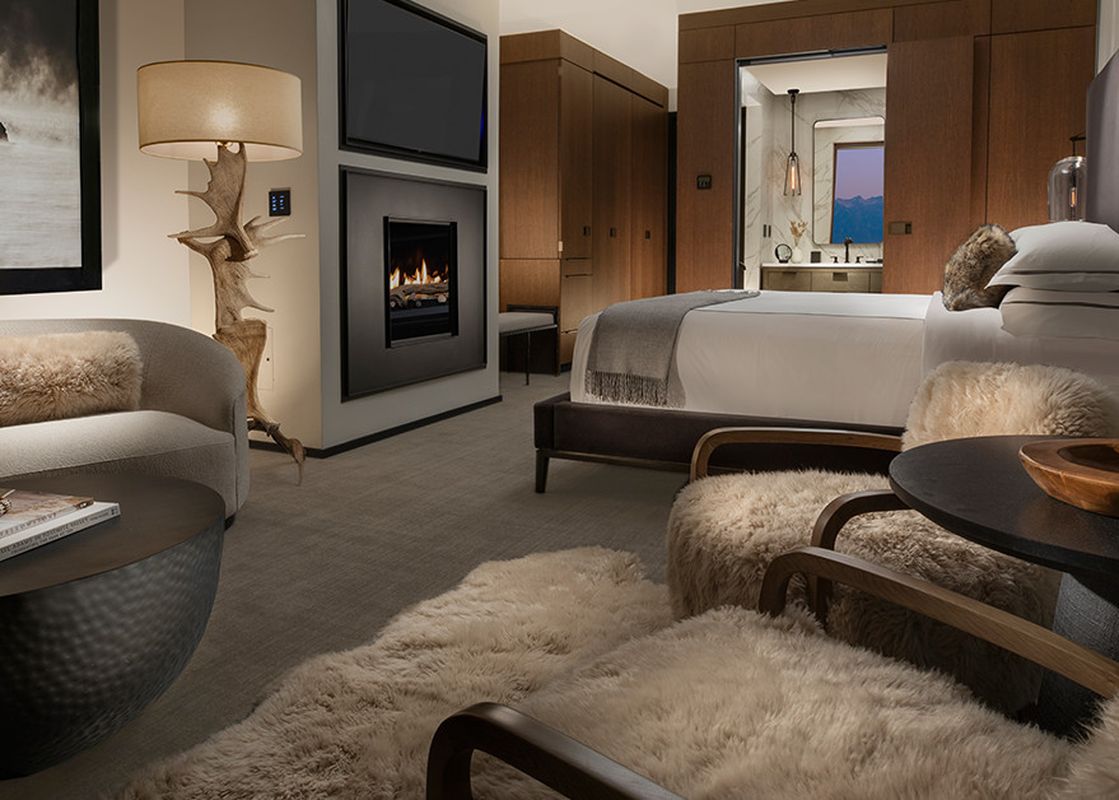 A luxurious and cozy suite, Reflection Suite Yellowstone, featuring a fireplace, a comfortable bed, a stylish sofa, and unique antler floor lamp.
