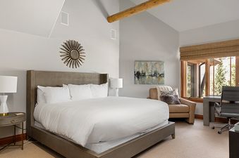 A hotel bedroom with a king-size bed, a large window with a view of the mountains, and a comfy armchair.