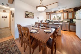 The dining area and kitchen of Hi Country Haus 1618, featuring a wooden dining table set for six with a centerpiece, and a fully equipped kitchen with modern appliances.