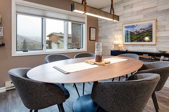 A modern dining area at the Ranch at Steamboat RA511 with a round wooden table, gray chairs, and a window offering a snow-covered mountain view.