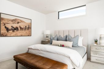 Moonlight Basin 8C Speedwell bedroom with a king-size bed, bedside tables, and a large window. The bed is dressed in white linens with blue pillows, and there is a brown leather bench at the foot of the bed.