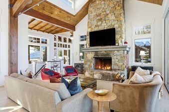 The luxurious great room at Snow Dance at The Colony featuring a grand stone fireplace and vaulted wood ceilings.