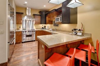 The image shows the kitchen of Silver Star 702, featuring stainless steel appliances, wooden cabinetry, granite countertops, and a breakfast bar with red stools.
