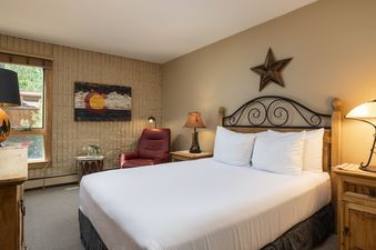 A bedroom at Vail 21 307 with a Colorado flag art piece on the wall, a bed with white linens, and a red armchair.