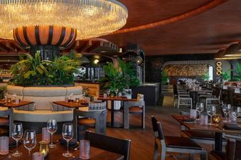 A modern dining room with a large chandelier, dark wood tables, and plush leather chairs.
