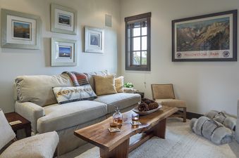 A cozy living room featuring a plush sofa with decorative pillows and a throw blanket, a rustic wooden coffee table with drinks, and framed artwork on the walls.