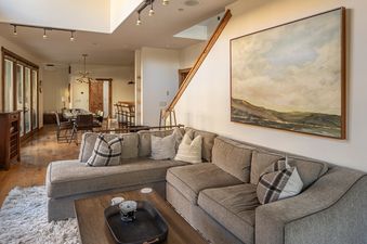 A spacious lounge area in Essentia Townhome 151B with a large L-shaped gray sectional sofa, a coffee table, and a dining area with a breakfast bar.