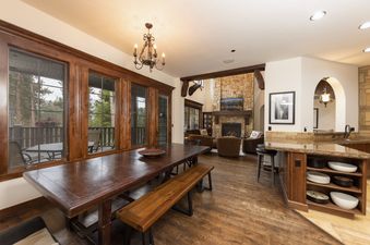 The dining area and living room with a stone fireplace and view of the forest.