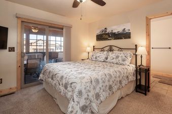 A cozy bedroom with a large bed, floral bedding, and a sliding glass door leading to a balcony with outdoor seating.