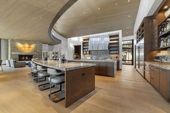 An expansive open-concept living space features a modern kitchen, a large island with bar seating, and a cozy living area with a stone fireplace.