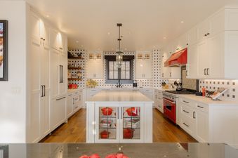 A modern kitchen with white cabinets, a large island, and red appliances, featuring a black and white patterned backsplash.
