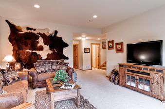 The inviting living area at His High Place features a blend of rustic charm and modern comfort, with plush leather sofas, a unique cowhide wall accent, and a large flat-screen TV.