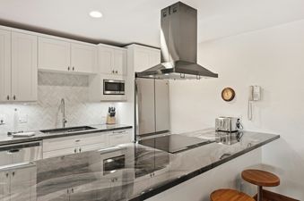 A modern kitchen with stainless steel appliances, white cabinets, and a black granite countertop.