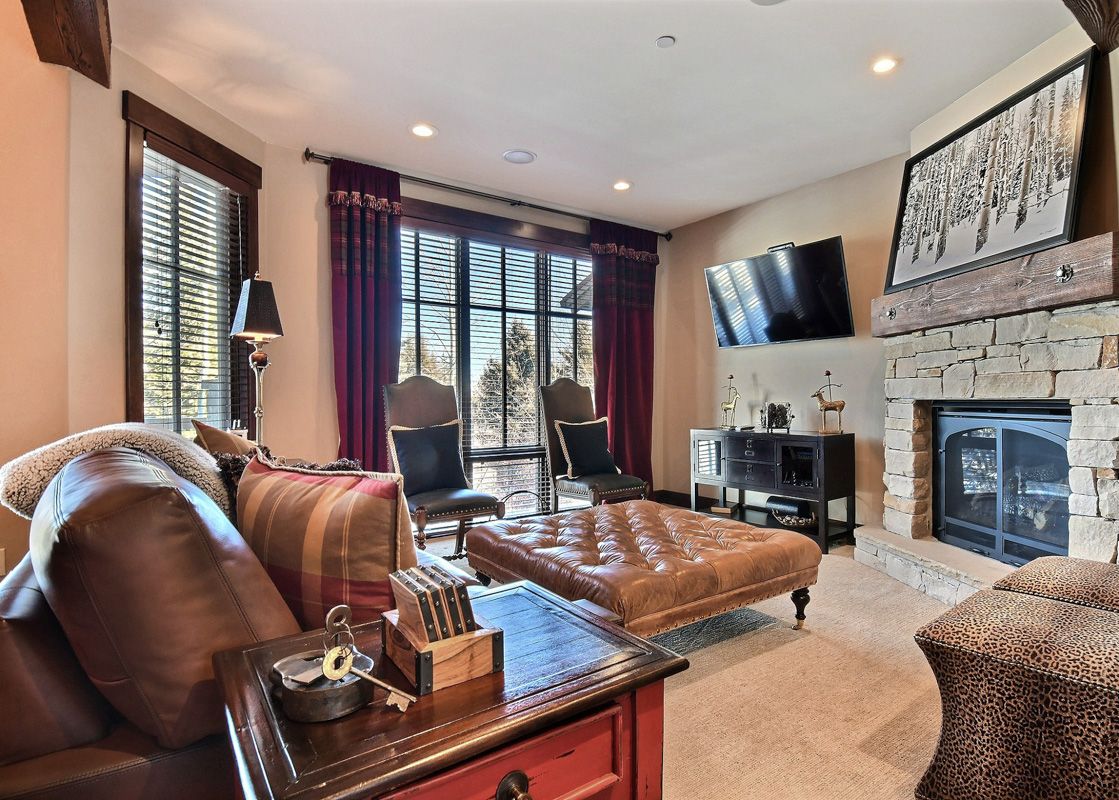 A cozy living room in Silver Star 903 with a fireplace, comfortable leather furniture, and a large window looking out onto trees.