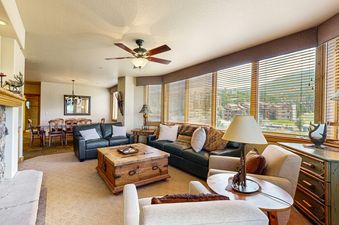 The living area within Torian Plum Creekside 519 features comfortable seating, a fireplace, and a dining area, with large windows overlooking the scenic outdoors.