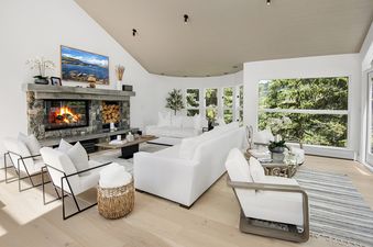 A bright and modern living room at Rockledge 325 with a stone fireplace, white sofas, and large windows overlooking lush greenery.