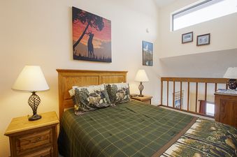 A cozy bedroom with a wooden bed, two nightstands with lamps, and a wall painting of a deer.