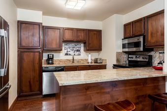 The Chateau Christian 2 Bedroom Platinum Unit 210 features a fully equipped kitchen with wooden cabinetry, stainless steel appliances, and a granite countertop island.