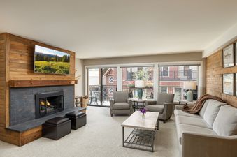 The inviting living area at Montaneros 320 features a cozy fireplace, a flat-screen TV, comfortable seating, and a balcony with an outdoor view.
