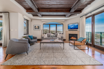 Lumiere Three Bedroom Luxury living room with grey couches and a coffee table. The room has hardwood floors, a fireplace, and a large window with a view of the mountains.