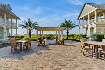 An expansive outdoor patio area at Palmilla Pearl with seating, fire pit, and pergolas, flanked by vacation homes and overlooking a golf course under a clear blue sky.