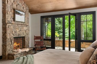 Master bedroom at Teton Crest featuring a stone fireplace and glass doors opening to a private patio.