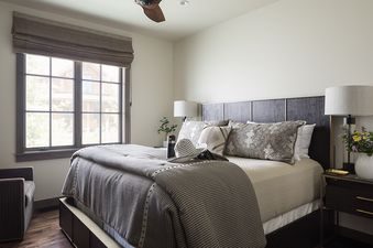 A luxurious bedroom at Lodge at Shooting Star 03 features a large bed with neutral bedding, dark wood furniture, and a window with a view of the outdoors.