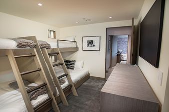 The Clubhouse is a spacious bedroom with a bunk bed that offers comfortable sleeping arrangements for multiple people, a flat-screen TV mounted on the wall, and a desk, offering ample space to relax and work.