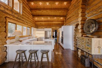 The Hang Glider Hideout's kitchen, featuring wooden log walls, white cabinetry, and stainless steel appliances, with a kitchen island and bar stools.