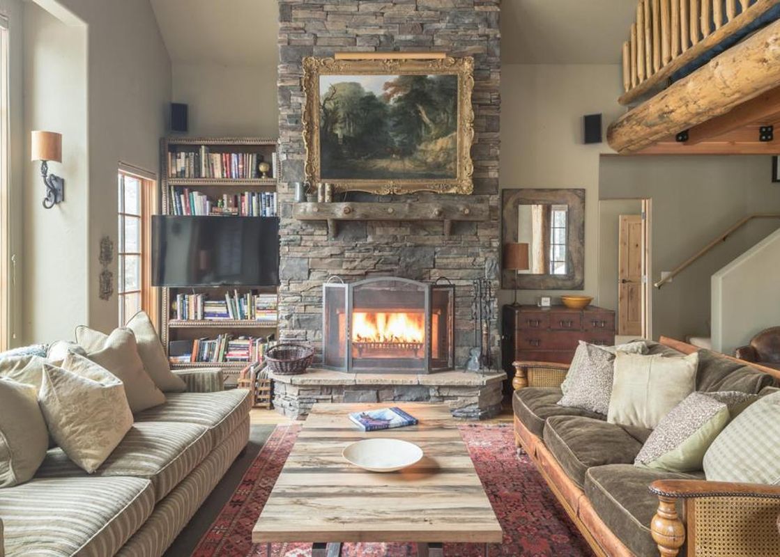 A cozy living room at Moonlight Mountain 2 Lower Mountain Road featuring a large stone fireplace with a painting above, two comfortable sofas, a wooden coffee table, and a bookshelf with a TV.
