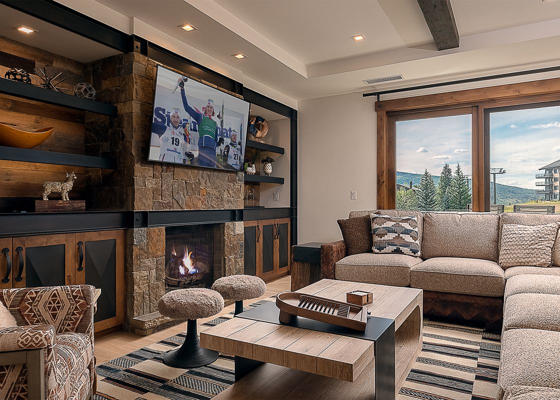 Modern mountain living room at Emerald Mountain One Steamboat Place 702 featuring a large stone fireplace, cozy sectional sofa, and scenic mountain views.