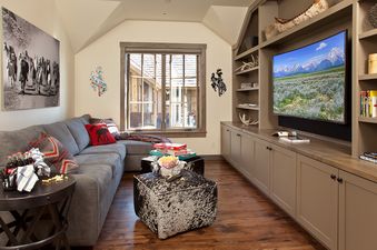 A cozy entertainment room at Fish Creek Lodge 02 with a large sectional sofa, a flat-screen TV in a built-in unit, and rustic decor.