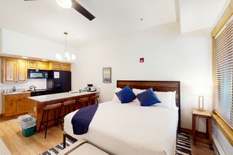 A cozy studio apartment at EagleRidge Lodge 313 features a queen bed, a fully equipped kitchen with modern appliances, and a breakfast bar with three stools.