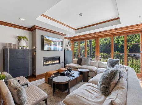 Bright and spacious living room at Alpine at the Ritz Carlton featuring a cozy fireplace, comfortable sectional, and large windows looking out onto a dense pine forest.