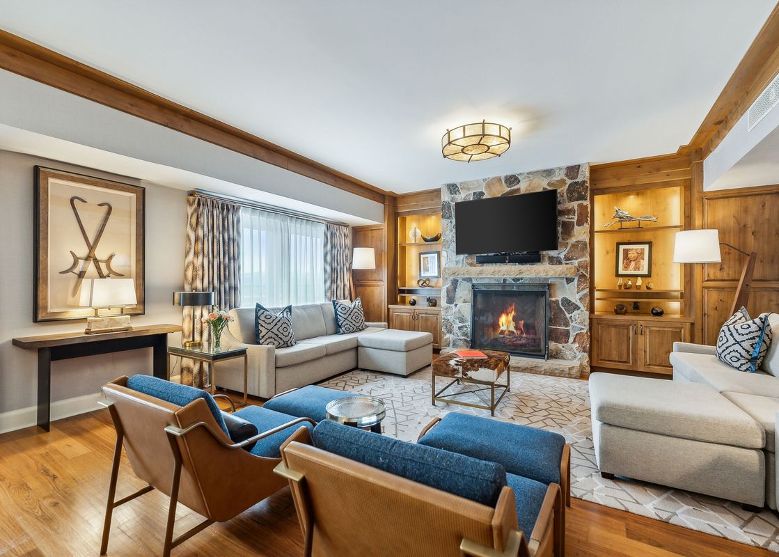 A spacious and inviting living room in the St Regis Executive Suite features a large stone fireplace, a comfortable sectional sofa, and elegant wooden furnishings.