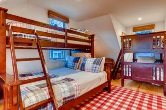 Two wooden bunk beds with plaid bedding, and a red and white checkered rug on a light wood floor.