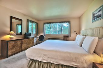 A master bedroom in Snow Flower 148 with a king-size bed, dresser, mirror, desk, and windows offering an exterior view of trees.