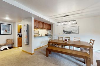 A spacious dining area with a long wooden table, chairs, and a bench, next to a well-appointed kitchen with wooden cabinets and modern appliances in Fallridge 204.