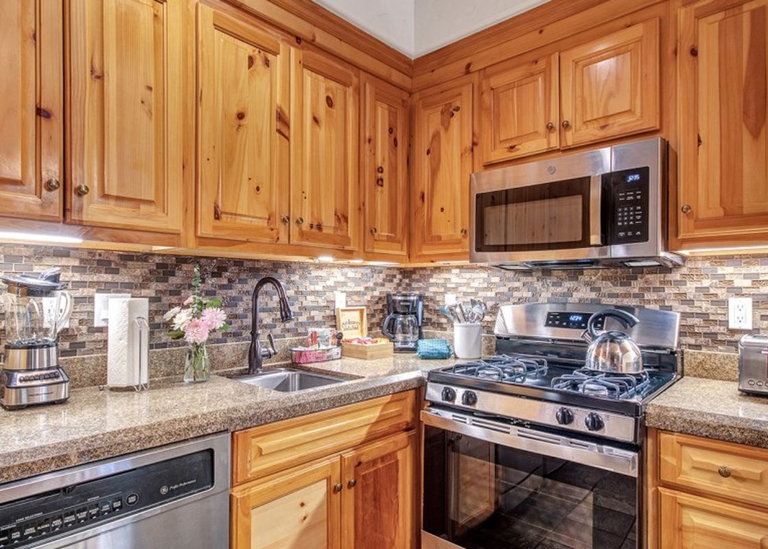 The Mountain Lodge 2 Bedroom Suite's kitchen features rich wooden cabinets, stainless steel appliances, and granite countertops, creating a warm and functional space.