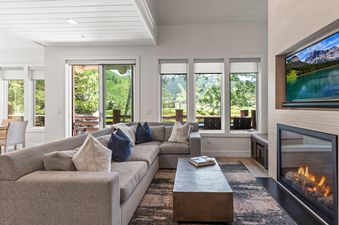 A cozy living room in Chaparral 204 features a plush sectional sofa, a modern coffee table, a flat-screen TV above a fireplace, and large windows revealing a vibrant green mountain landscape.
