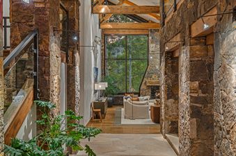 A hallway with a stone wall and a view of a living room with a fireplace.