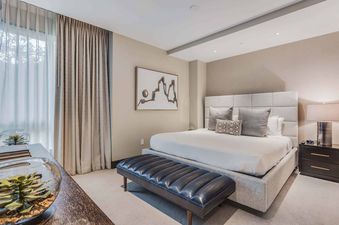 A modern master bedroom at One Snowmass East 304 features a king-size bed with an upholstered headboard, flanked by a dark wood nightstand with a lamp and an alarm clock.