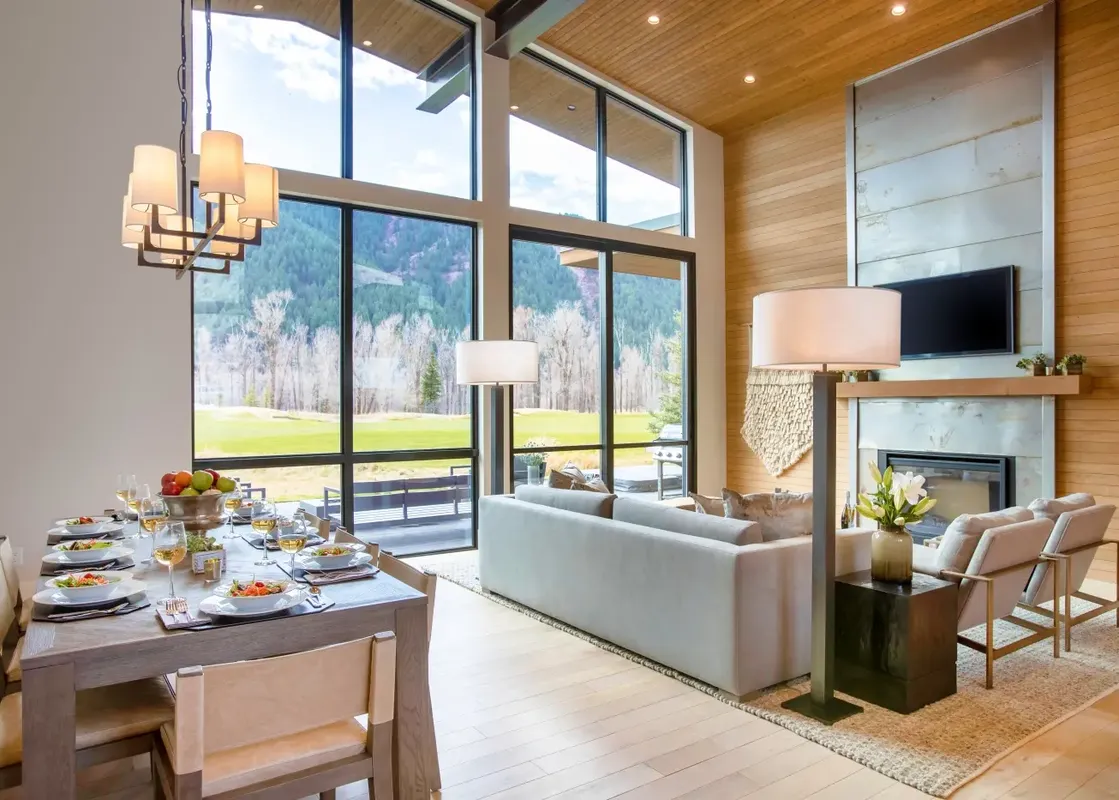 A luxurious open-plan living and dining area in The Lodge Cabins, featuring a fully set dining table, a comfortable lounge area with a fireplace, and large windows showcasing mountain views.