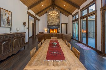 The dining area and living room of the Stony Creek Chalet feature a long wooden dining table, a stone fireplace, and large glass doors leading to a deck.