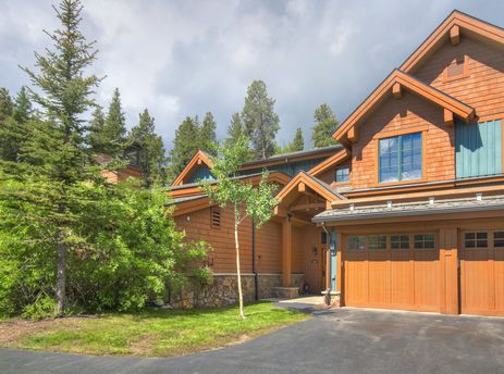 Exterior view of Mountain Thunder 2 Bedroom TH featuring wood siding, double garages, and surrounding pine trees.