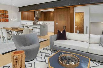 The living room of 1175 A Casolar Del Norte features a comfortable sofa, a swivel chair, a coffee table, a dining table, and a view of the kitchen with a stainless steel range hood and a granite countertop.