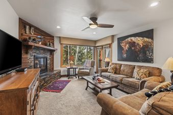 The living room at Snow Flower 56 Park City features comfortable seating, a stone fireplace, and large windows with beautiful outdoor views.