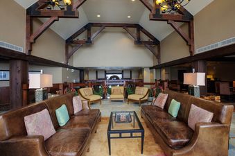 A spacious and inviting common area, part of the Crystal Peak 2 Bedroom, features comfortable seating, a glass coffee table, and an open layout with high ceilings and decorative wooden beams.