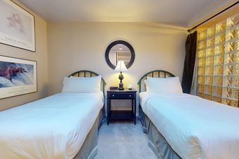 A cozy bedroom with two twin beds separated by a nightstand with a lamp and mirror above it.