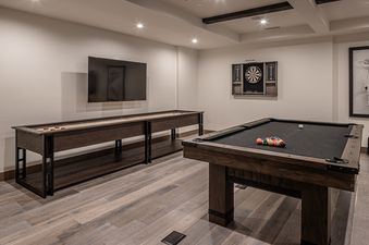 The game room at Inspiration Point Townhome 4C features a shuffleboard table, a wall-mounted TV, a pool table with billiard balls, and a dartboard.